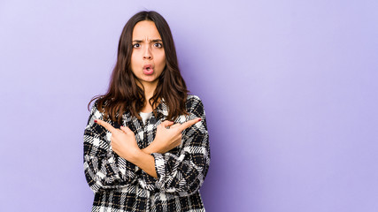 Young mixed race hispanic woman isolated points sideways, is trying to choose between two options.