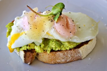 Avocado toast with a poached egg, cheese and a mustard leaf on a white plate