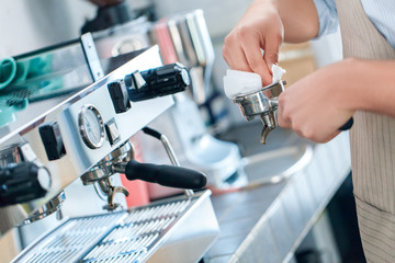 Young adult barista working in restaurant, cleaning filter in coffee machine