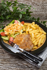 Fried pork chop in breadcrumbs, served with fries and salad.