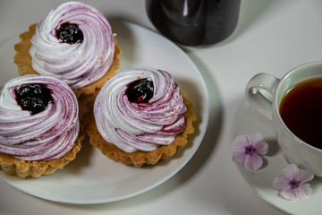 Sweet tartlet with meringue and blackberry jam and phlox flowers on white background closeup