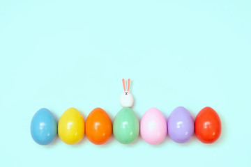 Top view of an Easter composition of painted eggs in bright juicy colors on a blue background with a little rabbit. Holiday concept, flat layout, minimalism