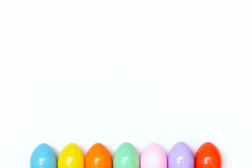 Top view of an Easter composition of painted eggs in bright juicy colors on a white background with a glossy texture. Holiday concept, flat layout, minimalism