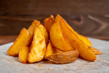 Rustic fried potatoes on paper and wooden background.