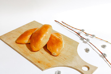 Three baked pies lie on a wooden cutting Board. On a white background decorated with willow branches