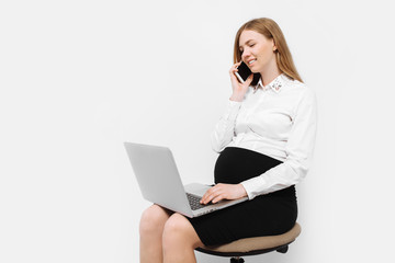 Image of a young pregnant businesswoman in glasses, a girl talking on the phone and working with a laptop, sitting on a chair