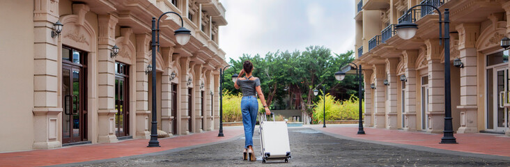A girl with a suitcase is walking down the street of the European quarter. Rear view. Panoramic photo. Concept of leisure and travel.
