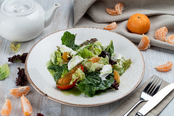 Italian salad with tangerine, greens, feta cheese and beefsteak tomato on white wooden table with ingredients around