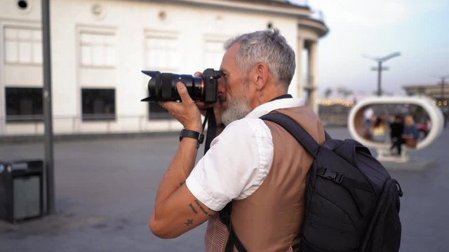 Photographer Traveller With Black Backpack Takes Aim To Take A Picture Of The City Building During The Trip