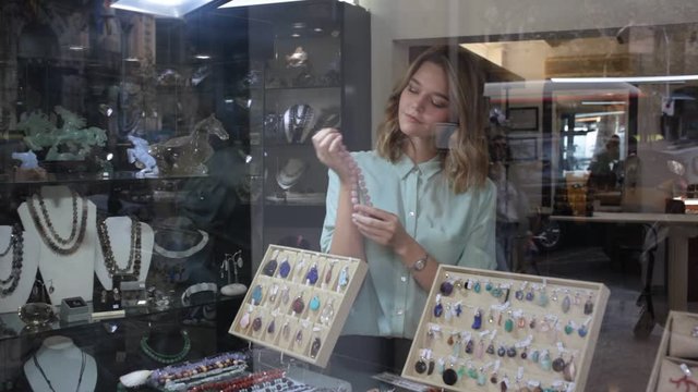 Portrait of cheerful female shop assistant demonstrating necklace made of rhodonite stone 