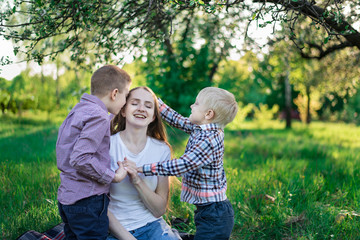 Loving mother playing with children. Two sons stroking mom's head. Picnic with family in nature.