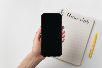 Female hand holds the phone. Pen and notebook with words New job. White background copy space