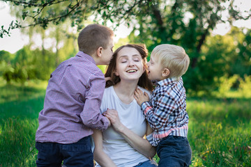 Naklejka na ściany i meble Little sons kiss mom on the cheek. Happy mother with two children in nature.