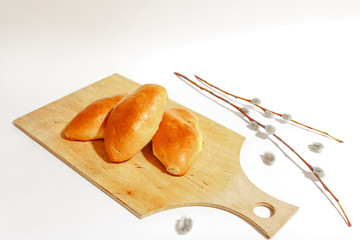 Three baked pies lie on a wooden cutting Board. On a white background decorated with willow branches