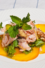 Front view, close distance of roasted beet salad with salmon, walnuts and mint in gold sauce on round, white plate