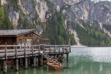 Fototapeta na wymiar landscape of Lago di Braies, impressive green lake, which reflects the high snowy mountains, surrounded by abundant green vegetation, we can also see a wooden cabin that is the jetty and some wooden b