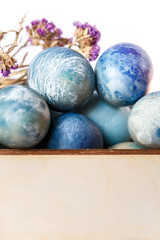 Easter colored eggs in a wooden box on white background. Easter eggs and spring flowers. Holiday pattern.