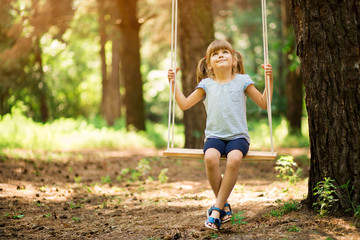 Happy Little girl on a swing in the summer park