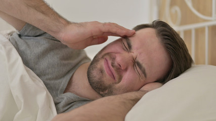 Fototapeta na wymiar Portrait of Young Man having Headache in Bed