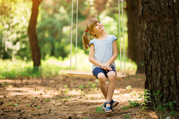 Happy Little girl on a swing in the summer park