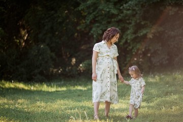 A beautiful young pregnant mom and her little daughter are picking flowers in a field. Motherhood. A family.