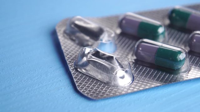 Blister pack of green purple medical capsules on a blue wooden table. Two capsules are missing. Pharmaceutical concept. Macro shot.