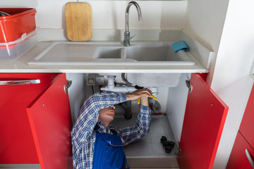 Male Plumber Fixing Sink In Bathroom