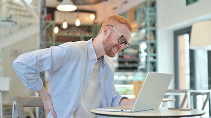 Redhead Man with Back Pain using Laptop in Cafe