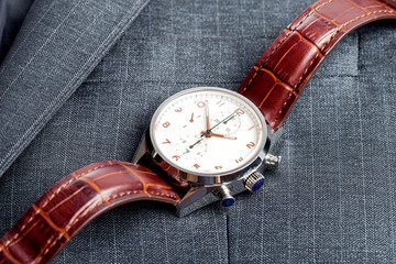man`s wristwatch of silver case and brown leather strap, close up lying watches with by the gray...