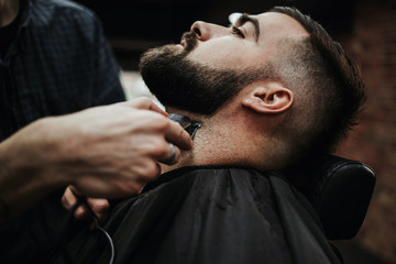 Obraz premium Good looking young adult man getting a hair and beard styling and dressing treatment by professional hairstylist.