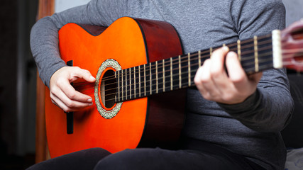 girl playing an orange acoustic guitar grips the chord on the fretboard. musical instrument lesson...