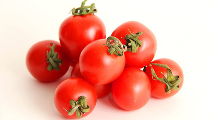 small red cherry tomatoes with green tails lie scattered on a white background