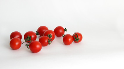 small red cherry tomatoes with green tails lie scattered on a white background