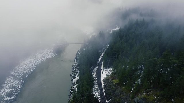 Fly over railroad in the cloudy mountain fores with the river and the bridge far away