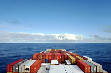 View on the containers loaded on deck of the large cargo ship. She is sailing through calm, blue...