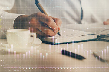 Double exposure of man's hands writing notes of stock market with forex chart.