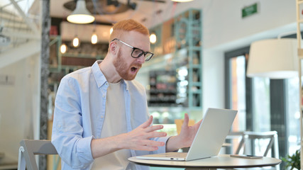 Redhead Man having Loss on Laptop in Cafe