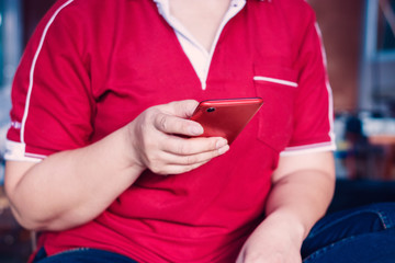 Stylish women wearing red shirts, relaxing on wooden chairs and playing Smartphone.