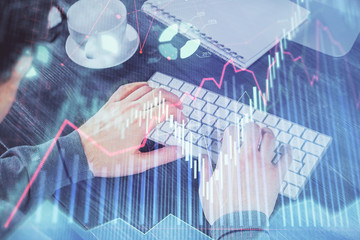 Double exposure of graph with man typing on computer in office on background. Concept of hard work.