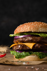 Homemade burger with grilled beef cutlet, sauce, vegetables and a glass of beer in the background. Copy space.
