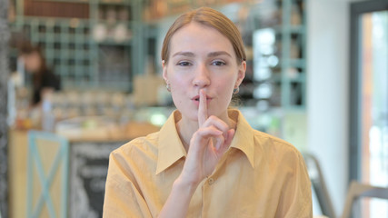 Fototapeta na wymiar Portrait of Young Woman Putting Finger on Lips, Quiet Sign