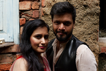 Fototapeta na wymiar Portrait of an young and attractive Indian Bengali brunette couple standing in front of a vintage brick wall wearing Indian traditional ethnic cloths. Indian lifestyle and fashion