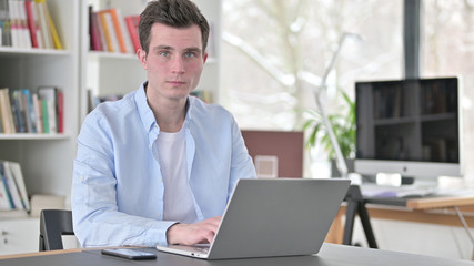 Fototapeta na wymiar Young Man Working on Laptop Looking toward Camera
