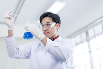A male Asian scientist wearing a white robe and looking at a glass tube Is a research about medicine in the laboratory. Concept, The scientist  with drug anti- Coronavirus or Covid2019.