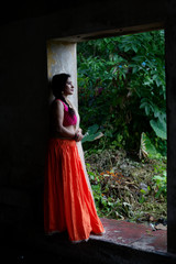 Young and beautiful Indian Bengali brunette woman is standing thoughtfully on the porch of a vintage house wearing Indian traditional ethnic vibrant skirt blouse. Indian lifestyle and fashion