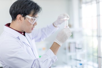 A male Asian scientist wearing a white robe and looking at a glass tube Is a research about medicine in the laboratory. Concept, The scientist  with drug anti- Coronavirus or Covid2019.