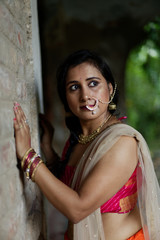 Fototapeta na wymiar Portrait of an Young and beautiful Indian Bengali brunette woman standing while holding a brick wall wearing Indian traditional ethnic vibrant skirt blouse. Indian lifestyle and fashion
