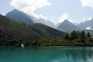 Fototapeta na wymiar lake in mountain valley, surface of water under rocky peaks, mountain surface on horizon, path to top and its achievement by river