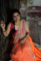 Portrait of an Young and beautiful Indian Bengali brunette woman sitting on the staircase of a vintage house wearing Indian traditional ethnic vibrant skirt blouse. Indian lifestyle and fashion