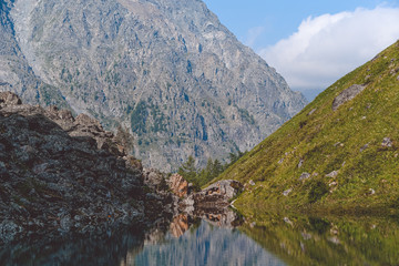 lake with peaks and rock ridge on horizon, hiking and climbing in mountains, stone cliff above blue water